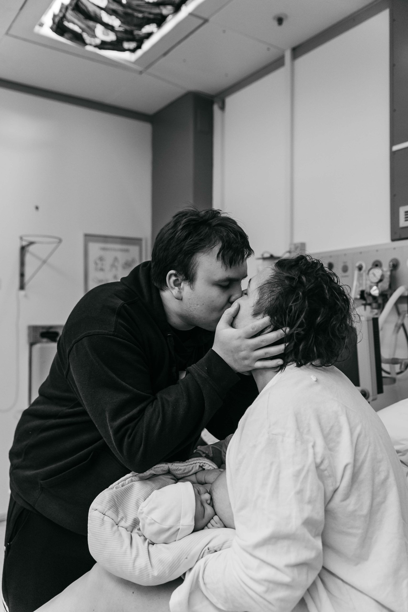 glade og trætte forældre kysser på hospitalet mens nyfødt baby ammes